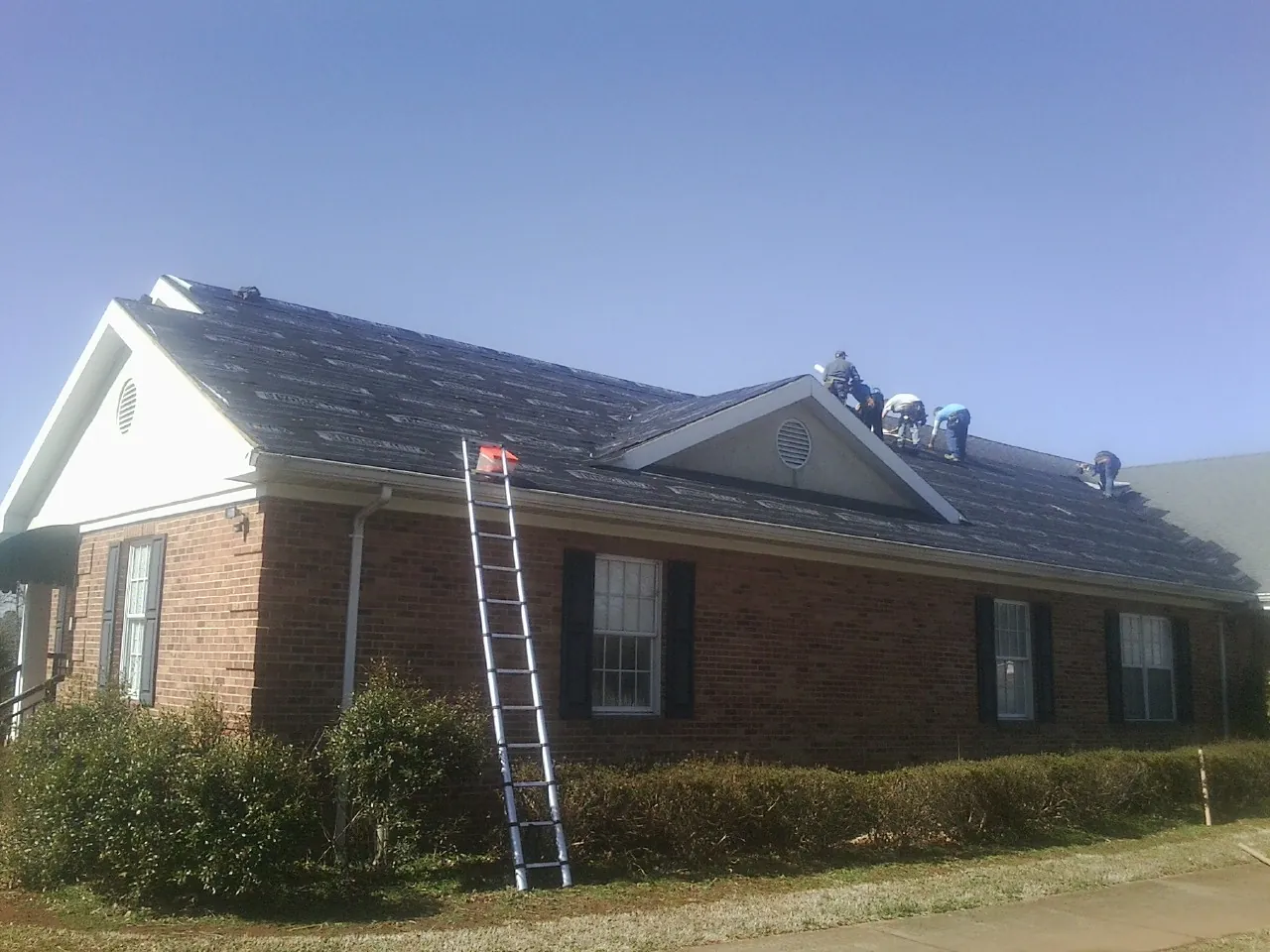Crew tearing shingles off a brick ranch roof with a ladder set — Metal Roof Repair work by our crew in Bruneau