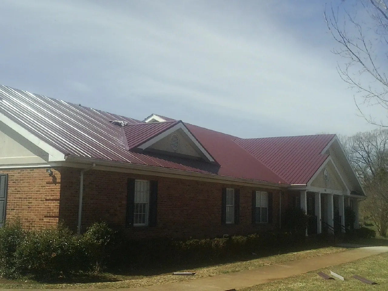 Red metal roof with gabled entries on a long brick building, from a Hail Damage Roof Repair job in Bruneau