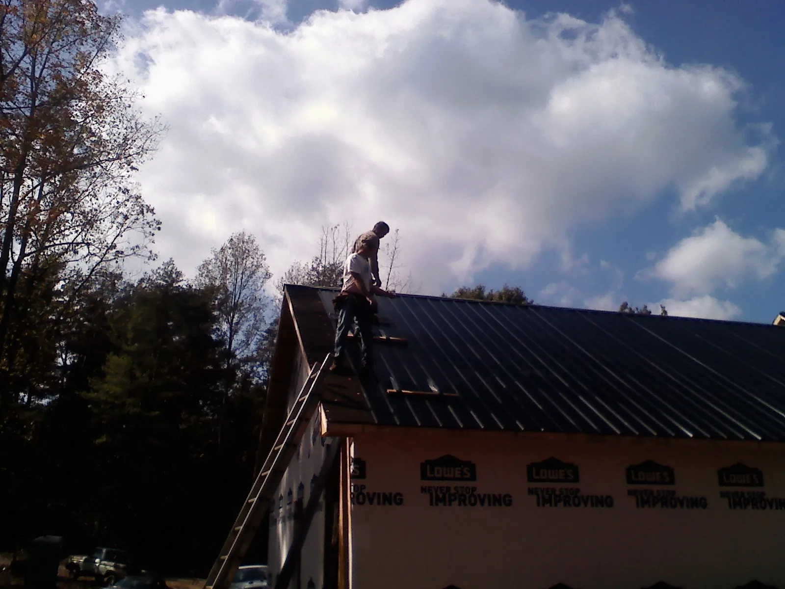 Roofer fastening dark metal panels high against a cloudy sky, from a Roof Inspection job in Bruneau