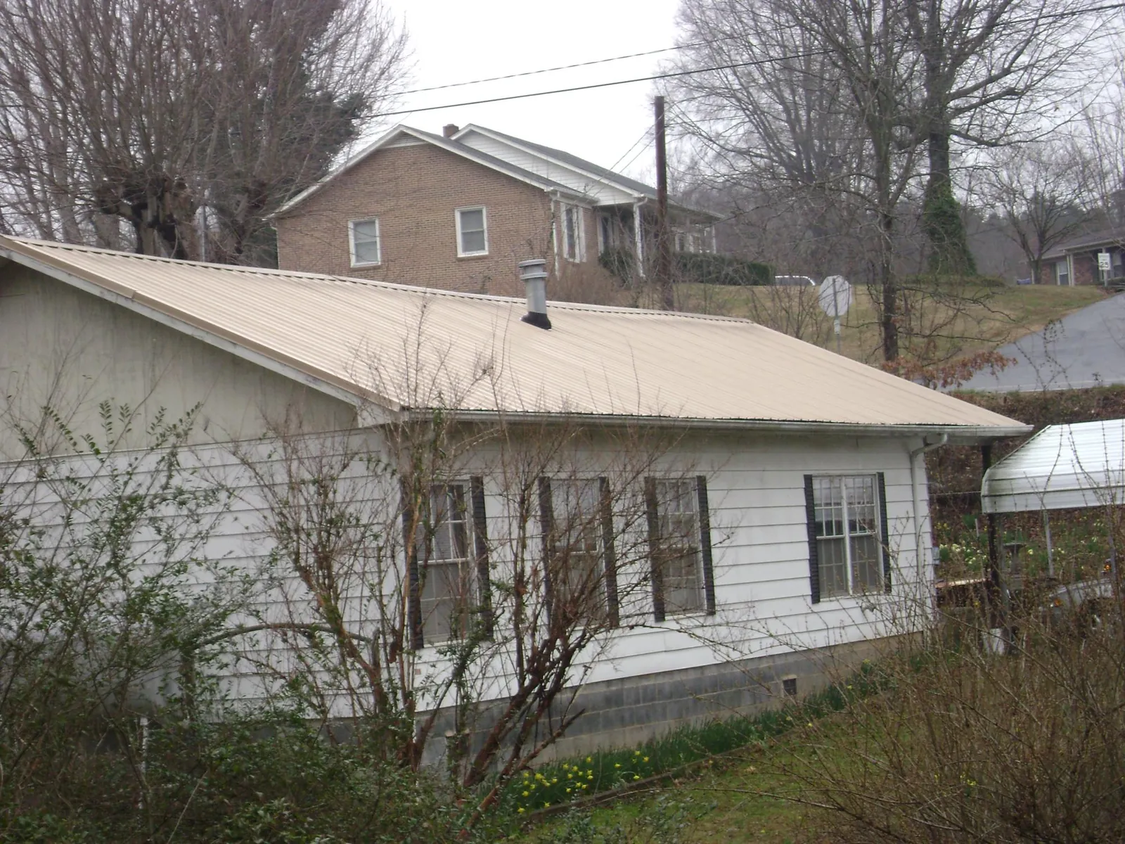 Tan metal roof on a white sided house set into a hillside — Commercial Roofing by Roofing Brothers in Bruneau